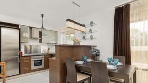 A modern kitchen with a central island, stainless steel appliances, and a dining area with a table set for four. - Spacious Apartment for 6 Persons | Parking | Workspace (Kraków)