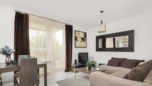 A modern living room with a sofa, a dining table with chairs, a TV, and a large window with curtains. - Spacious Apartment for 6 Persons | Parking | Workspace (Kraków)