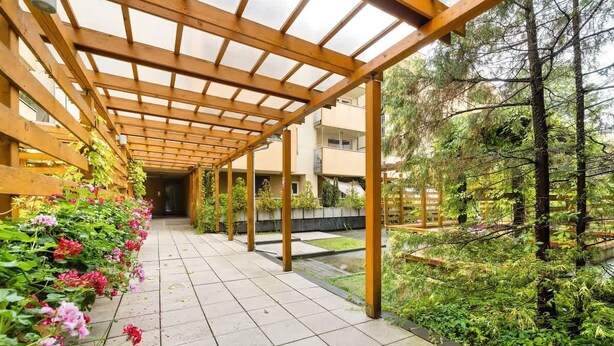 A covered walkway with a wooden pergola, surrounded by lush greenery and flowers. - Spacious Apartment for 6 Persons | Parking | Workspace (Kraków)