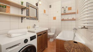 A modern bathroom with a Bosch washing machine, a toilet, a bathtub, and shelves with toiletries. - Spacious Apartment for 6 Persons | Parking | Workspace (Kraków)