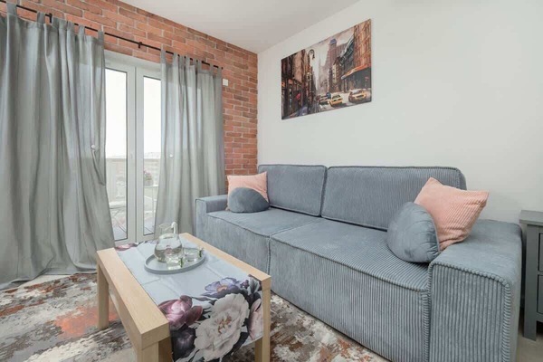 A bright living room with soft blue and grey seating, colorful pillows, and large windows.