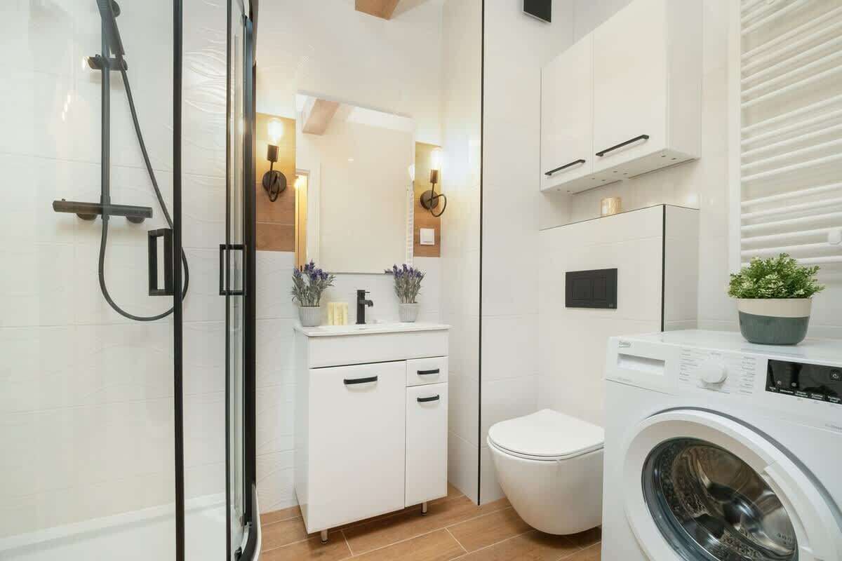 A modern bathroom with a glass shower enclosure, a white sink with a mirror, a toilet, and a front-loading washing machine.