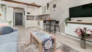 Ein modernes Wohnzimmer mit einer Couch, einem Couchtisch, einem Fernseher und einer Küchenzeile mit Schränken und einem Esstisch.