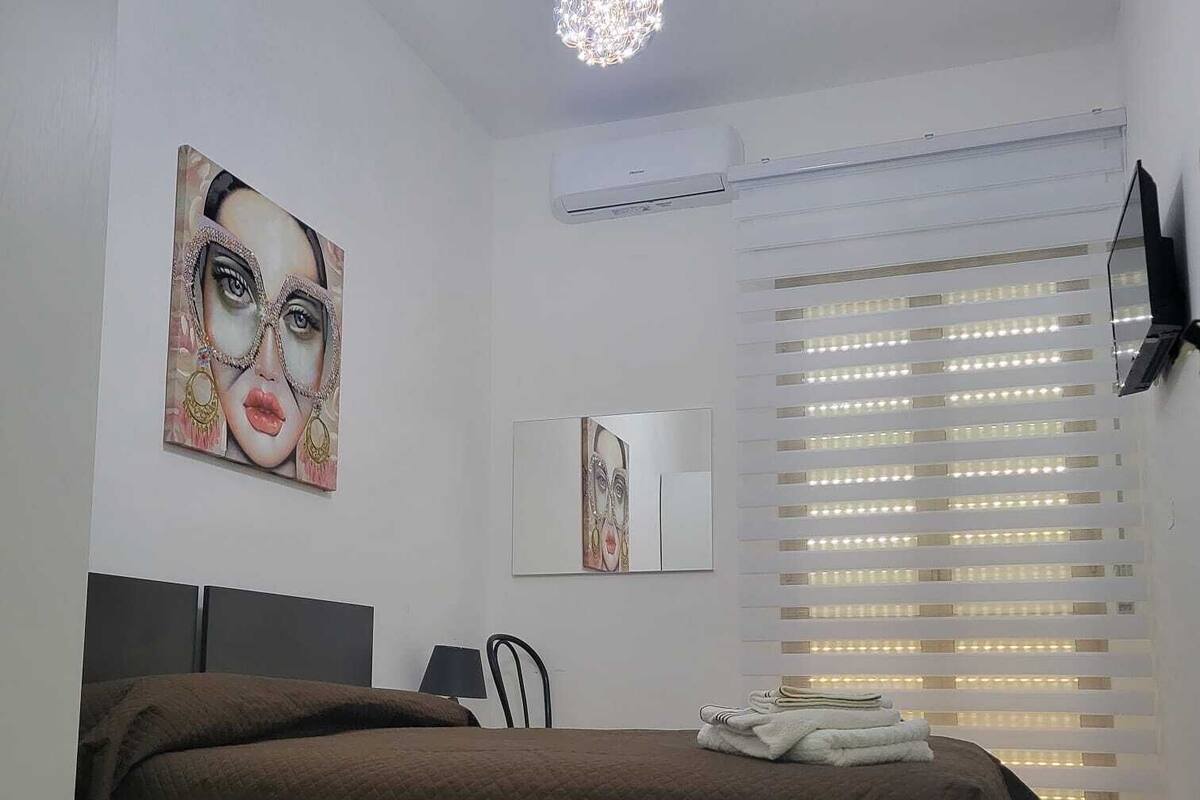 A bedroom with a bed, a desk, a chair, a TV, and artwork on the walls.
