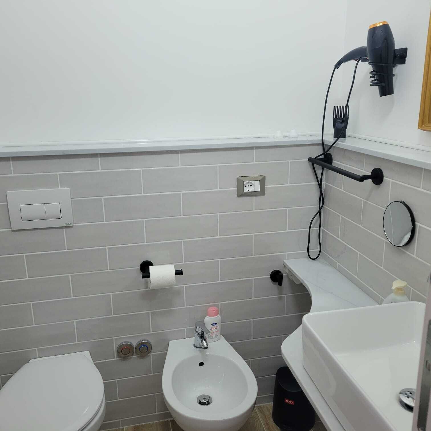 A bathroom with a toilet, bidet, sink, and a hairdryer mounted on the wall.