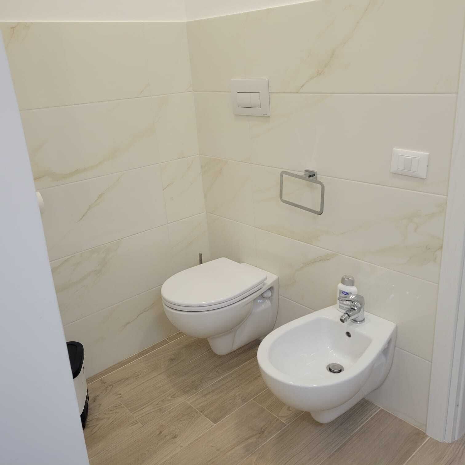 Um banheiro pequeno e moderno com vaso sanitário e bidê, paredes de mármore e piso de madeira.