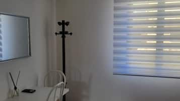 Ein Zimmer mit Bett, Schreibtisch mit Stuhl, Fernseher und einem Fenster mit Jalousien.