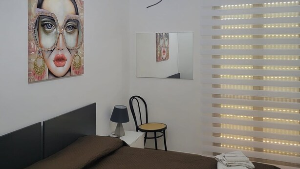 A modern bedroom with a bed, a chair, a desk, and a large window with blinds. - beb dei sogni (Cosenza)