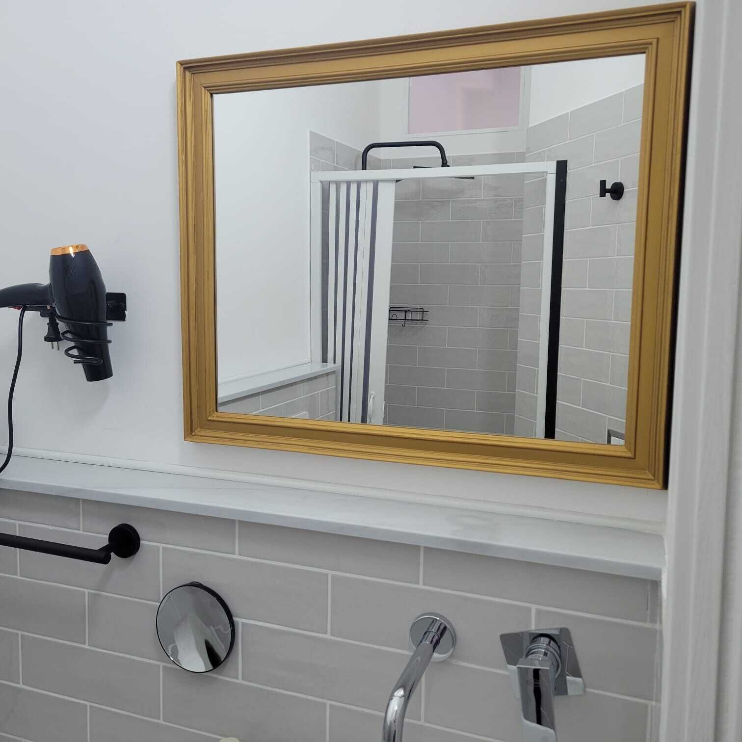 A bathroom with a large mirror, a hairdryer, a towel rack, and a shower control panel.