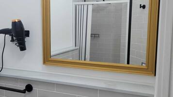 A bathroom with a large mirror, a hairdryer, a towel rack, and a shower control panel.