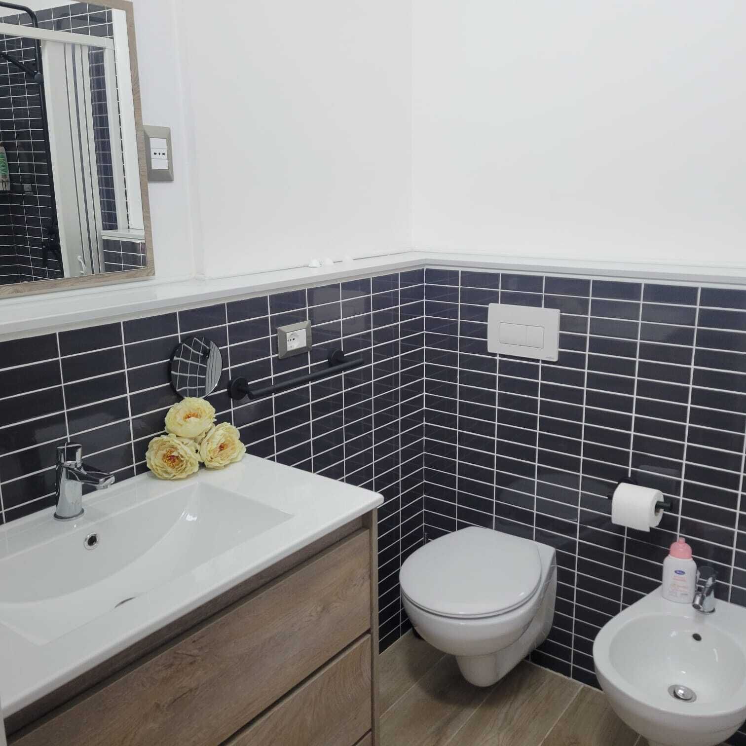 A bathroom with a white sink, a toilet, and a bidet. There are wooden cabinets below the sink and a mirror above it.