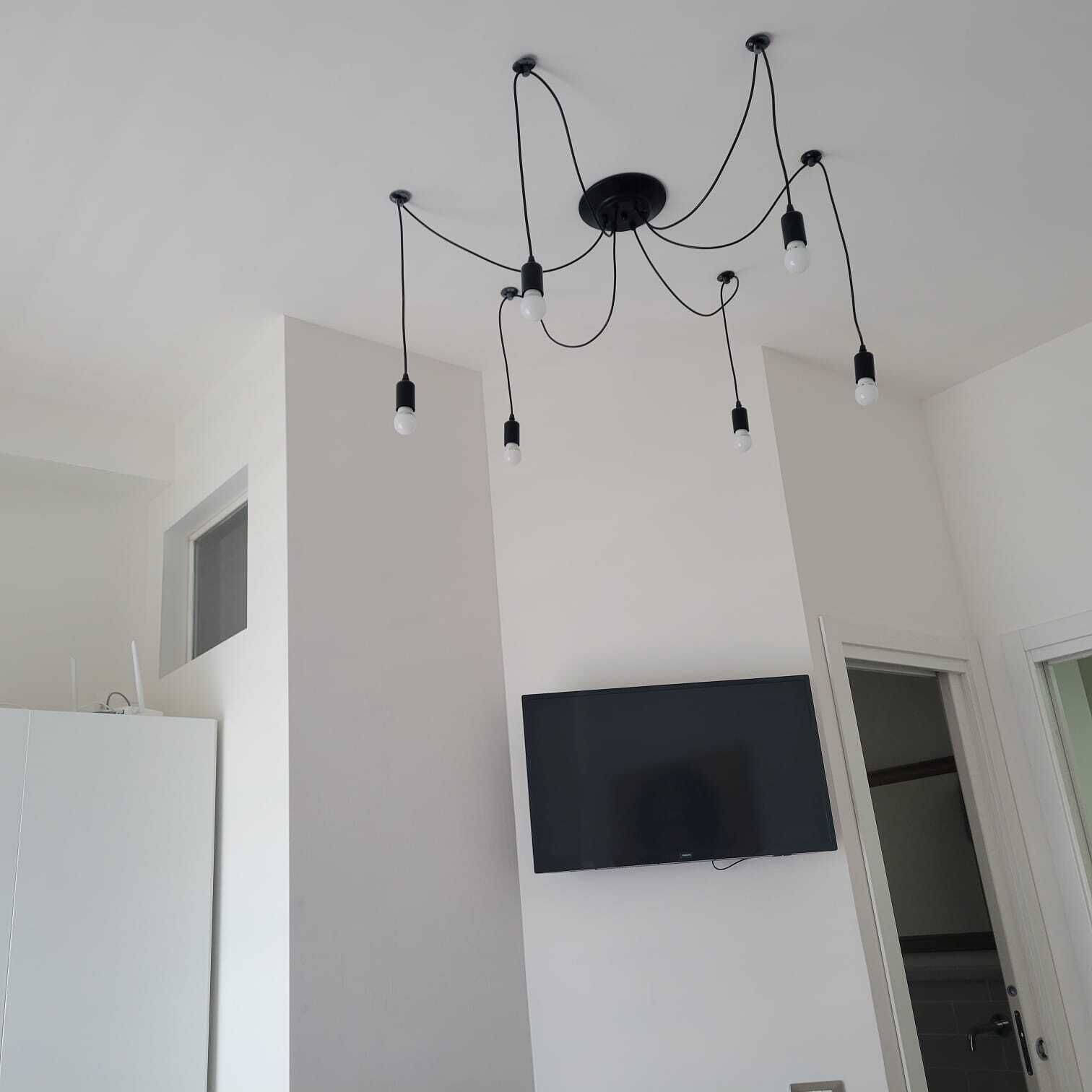 Una habitación moderna con candelabro en el techo, televisor de pantalla plana en la pared y armario blanco.