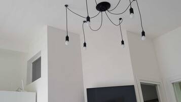 Una habitación moderna con candelabro en el techo, televisor de pantalla plana en la pared y armario blanco.