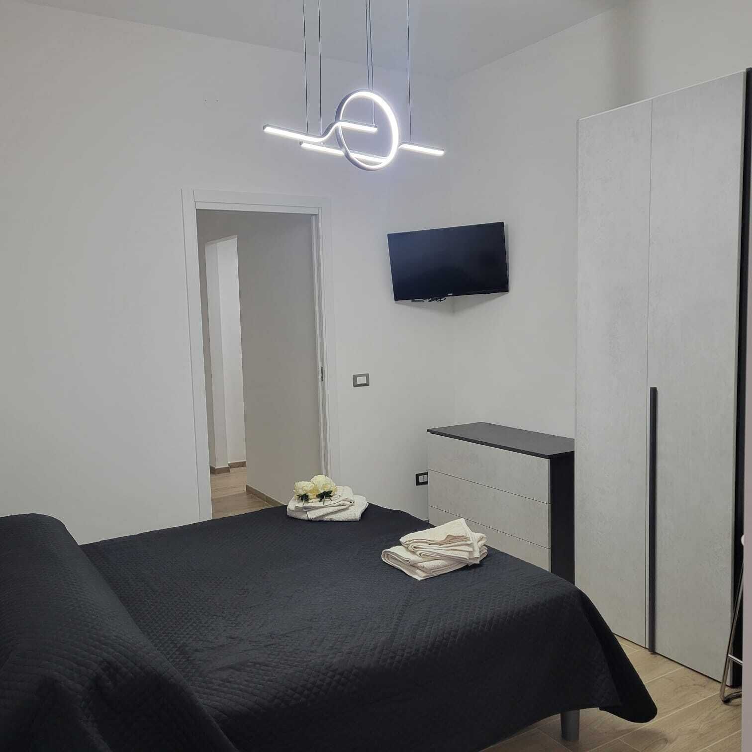 A modern bedroom with a bed, a TV mounted on the wall, a wardrobe, and a bedside table.