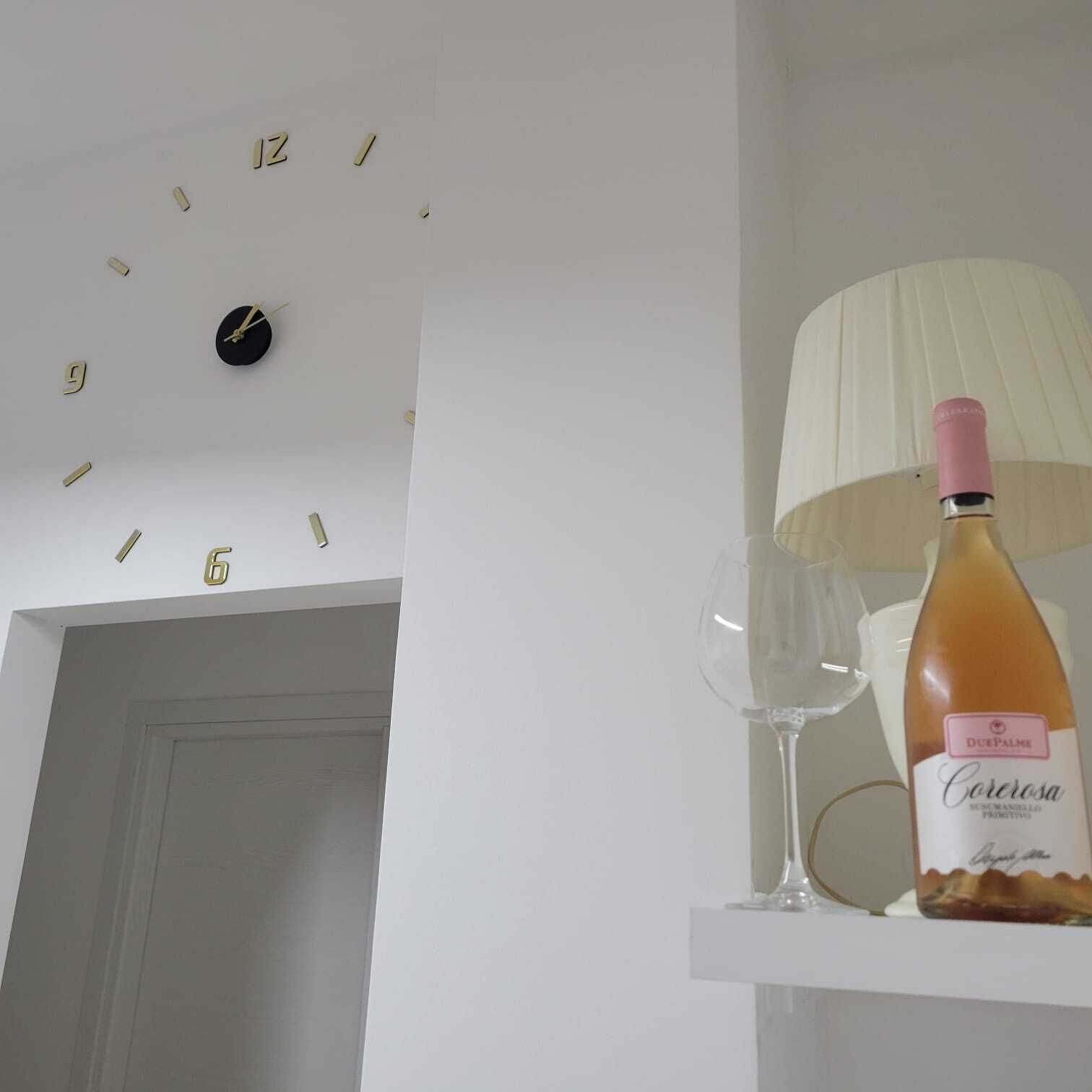 Ein Zimmer mit einer Wanduhr, einer Weinflasche und zwei Weingläsern auf einem Regal.