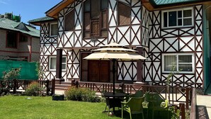 A traditional half-timbered house with a green lawn, outdoor seating, and a clear blue sky. - wildflower villa (Anantnag)