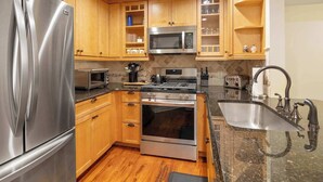 A modern kitchen with stainless steel appliances, wooden cabinets, and a granite countertop. - Inviting Ski-In/Ski-Out Condo at Okemo +Hot Tub (Ludlow)