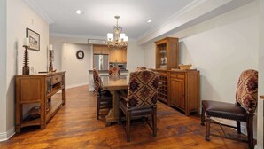 A dining area with a wooden table, two patterned chairs, a chandelier, and a kitchen in the background. - Inviting Ski-In/Ski-Out Condo at Okemo +Hot Tub (Ludlow)