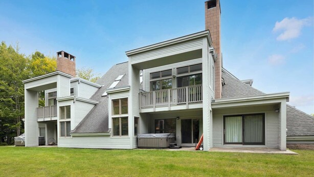 A two-story house with a balcony, large windows, and a chimney. - Inviting Ski-In/Ski-Out Condo at Okemo +Hot Tub (Ludlow)