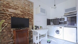 Cocina compacta con lavadora, microondas y televisor sobre un mueble de madera.