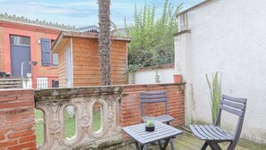 Un balcón con un muro de ladrillo, una pequeña mesa con una planta en maceta y dos sillas.