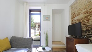 Una habitación con sofá, una mesita con una planta, un televisor sobre un mueble y una pared de ladrillo.