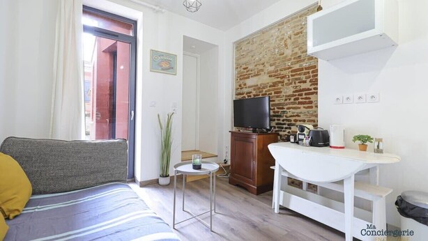 Un espacio habitable compacto con sofá, una mesita, televisor y pared de ladrillo.