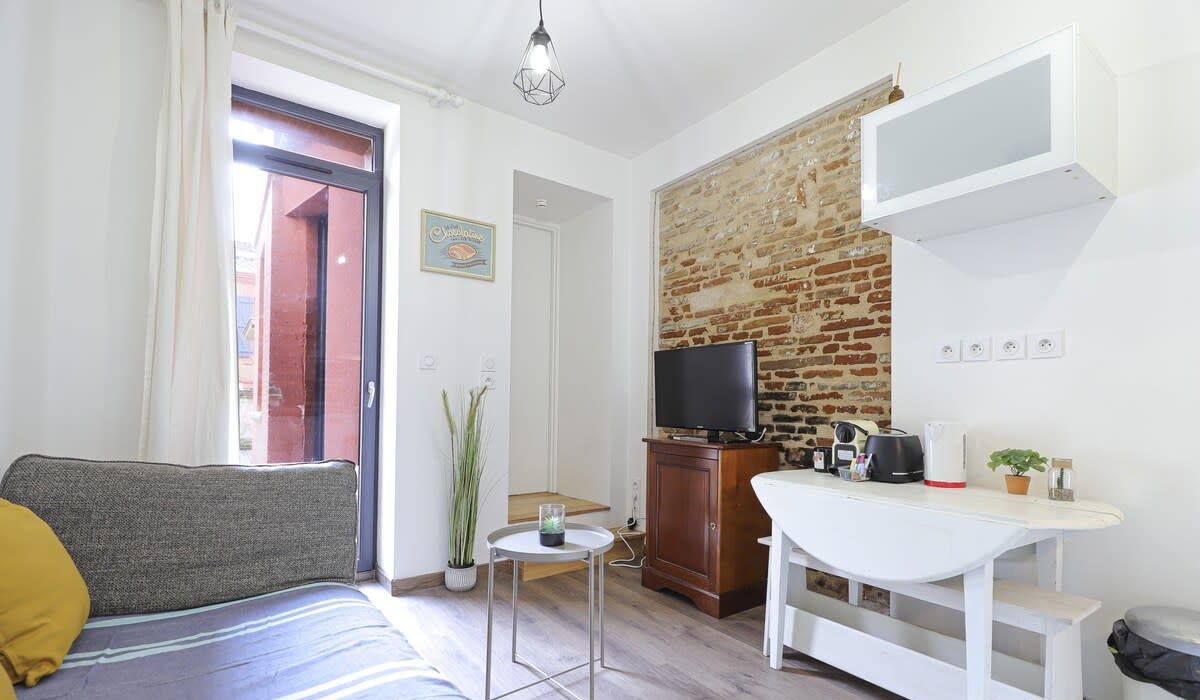 Un espacio habitable compacto con sofá, una mesita, televisor y pared de ladrillo.