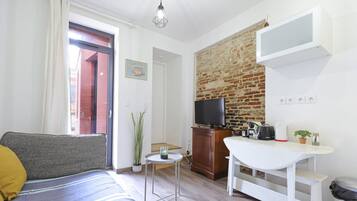 Un espacio habitable compacto con sofá, una mesita, televisor y pared de ladrillo.