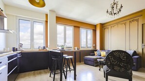 A modern kitchen with a central island, bar stools, and a dining area with a sofa and chairs.
