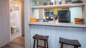 Een keuken met een wit aanrecht, houten krukken, een koelkast en een koffiemachine.