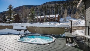 Un terrazzo in legno con una vasca idromassaggio, una cabina di legno e montagne sullo sfondo.