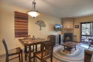 A dining area with a wooden table and chairs, a fireplace, and a large window with a view of trees.