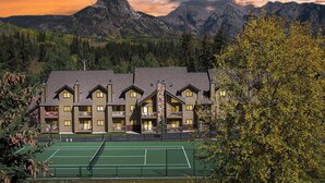 Un lodge con campo da tennis, circondato da montagne e alberi.
