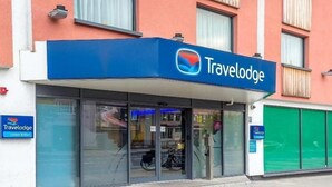 A Travelodge hotel with a blue sign, glass entrance, and a motorcycle parked outside.