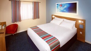A hotel room with a large bed, a red chair, a desk, and a window with curtains.