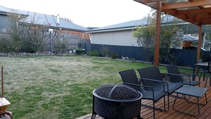 A wooden deck with outdoor furniture, a fire pit, and a view of a backyard with a lawn and a fence. - This is New England! (Armidale)