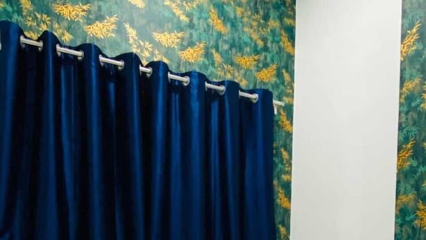 Ein Bett mit weißer Bettwäsche und einem blauen Kopfkissen, ein dunkelblauer Vorhang und eine Wand mit einem Blumenmuster.