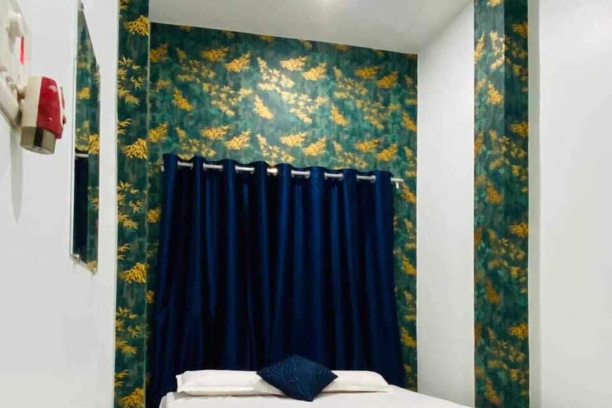 Une chambre à coucher avec un lit, des rideaux et un mur orné d’un motif floral.