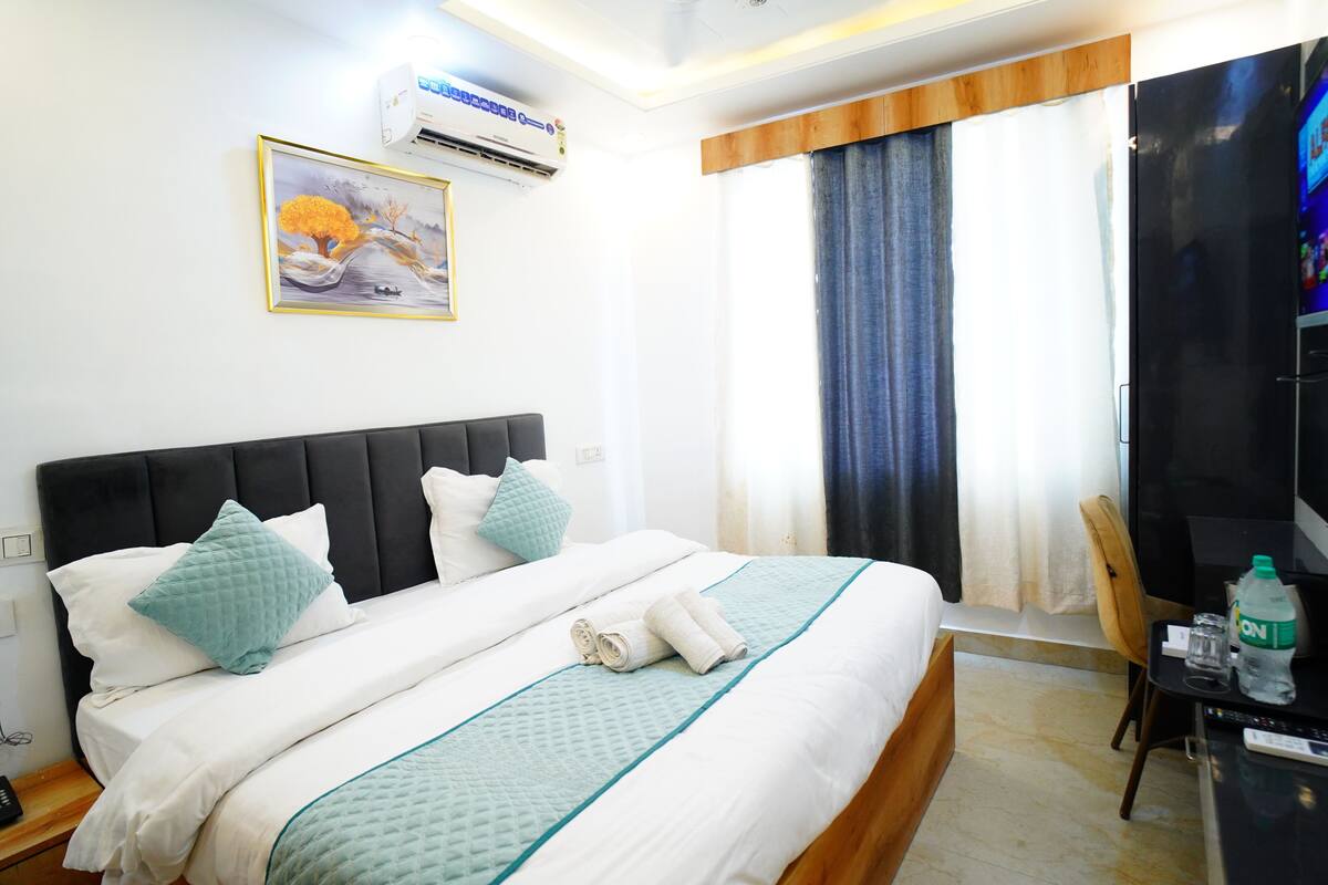 A hotel room with a bed, a TV, a desk, and a window with curtains.
