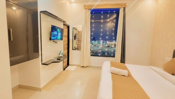 A modern hotel room with a bed, a TV, a desk, and a city view. - Hotel Devine  (Zirakpur)