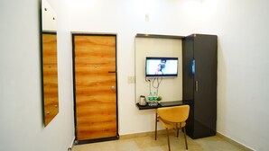 A room with a wooden door, a television mounted on the wall, a small table with a chair, and a refrigerator. - Hotel Devine  (Zirakpur)