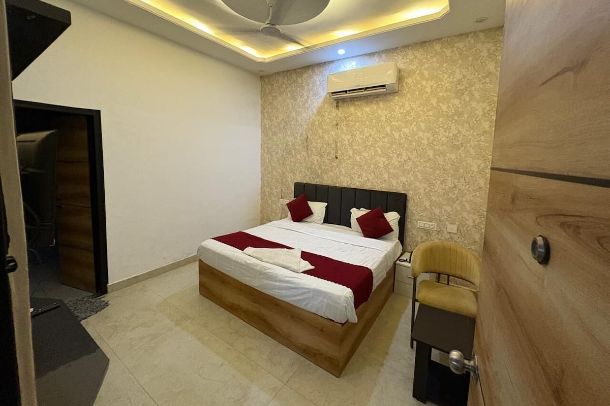 A bedroom with a bed, a ceiling fan, an air conditioning unit, and a wooden wardrobe.