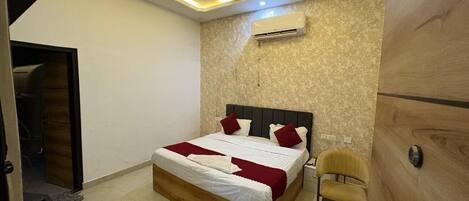 A bedroom with a bed, a ceiling fan, an air conditioning unit, and a wooden wardrobe.