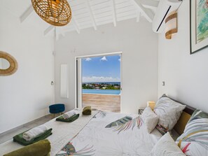 A bedroom with a large bed, a view of the sea, and a door leading to an outdoor area.