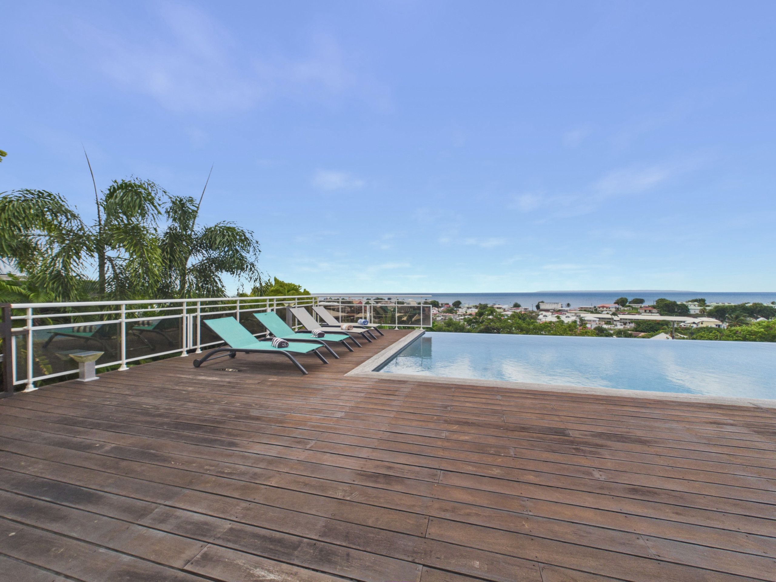 Une terrasse en bois avec des chaises longues et une piscine donnant sur une zone côtière.