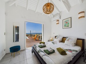 Un dormitorio con cama, una silla, una puerta y vista al océano.