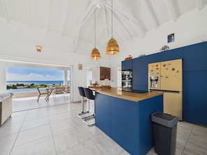 A modern kitchen with a view of the sea, a dining area with a table and chairs, and a trash bin.