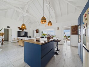 Una cocina moderna con una isla central, luces colgantes y vista al océano.