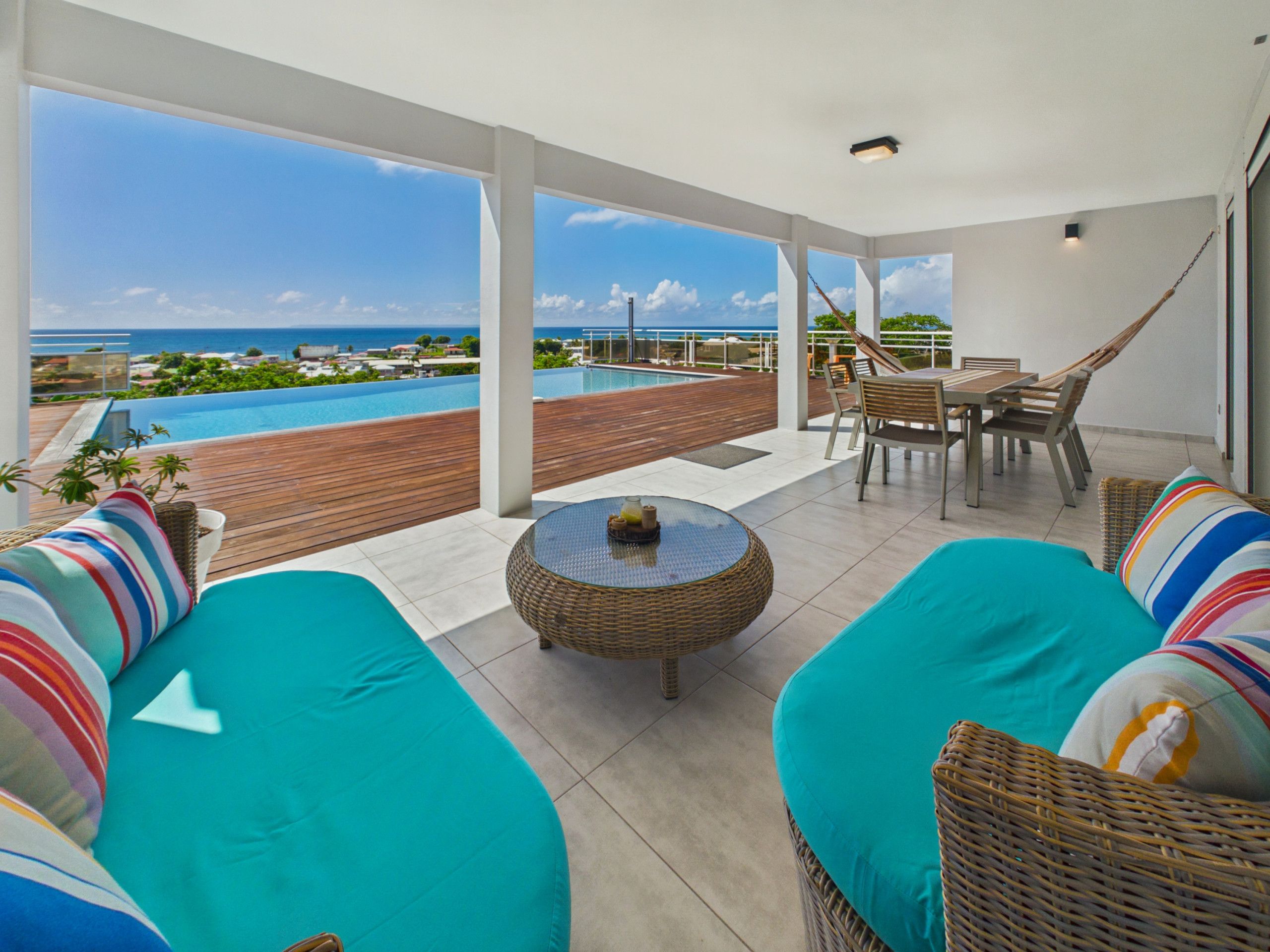 A sunlit patio with a view of the sea, a pool, and outdoor furniture.